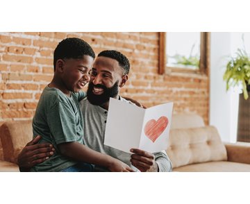 Far håller vitt kort med rött hjärta från son som sitter i hans knä