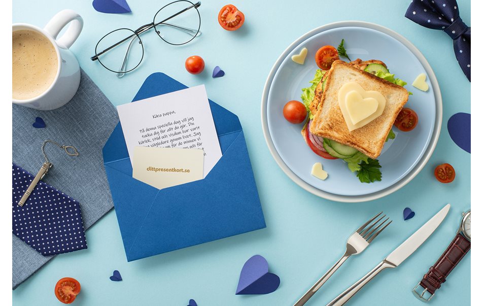Flatlay-bild av ett frukostbord med en tallrik med mat, glas, kaffe och ett kort för fars dag.