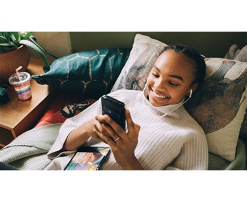Hög vinkelvy av leende tonårsflicka som lyssnar på musik medan du använder mobiltelefon på sängen hemma